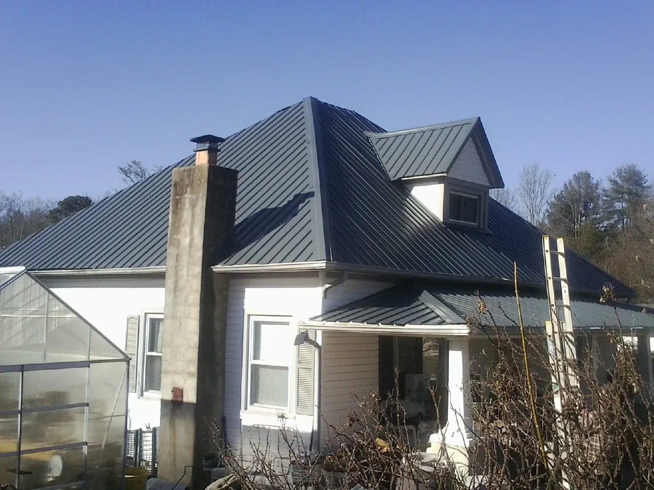 Dark blue standing seam metal roof on a white farmhouse with dormer — Slate & Tile Roof Repair by Roofing Brothers in Evansville