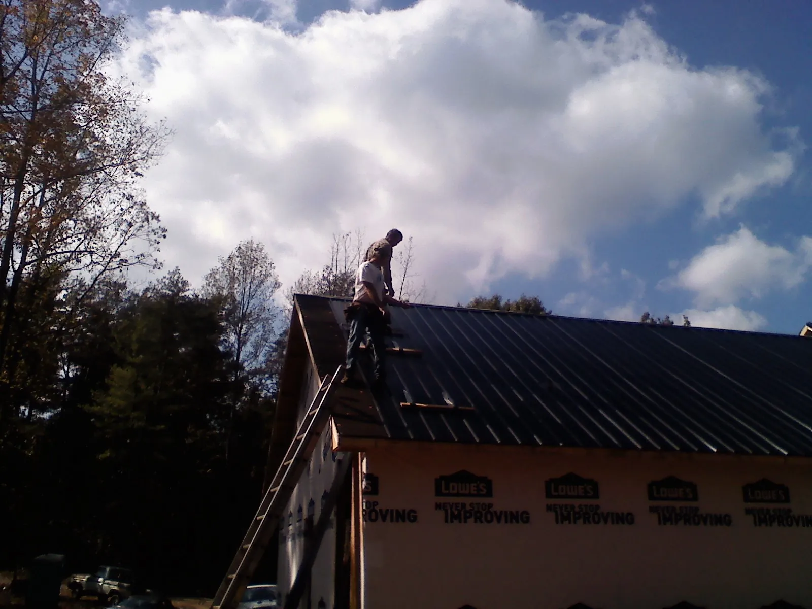 Roofer fastening dark metal panels high against a cloudy sky, from a Roof Inspection job in Evansville