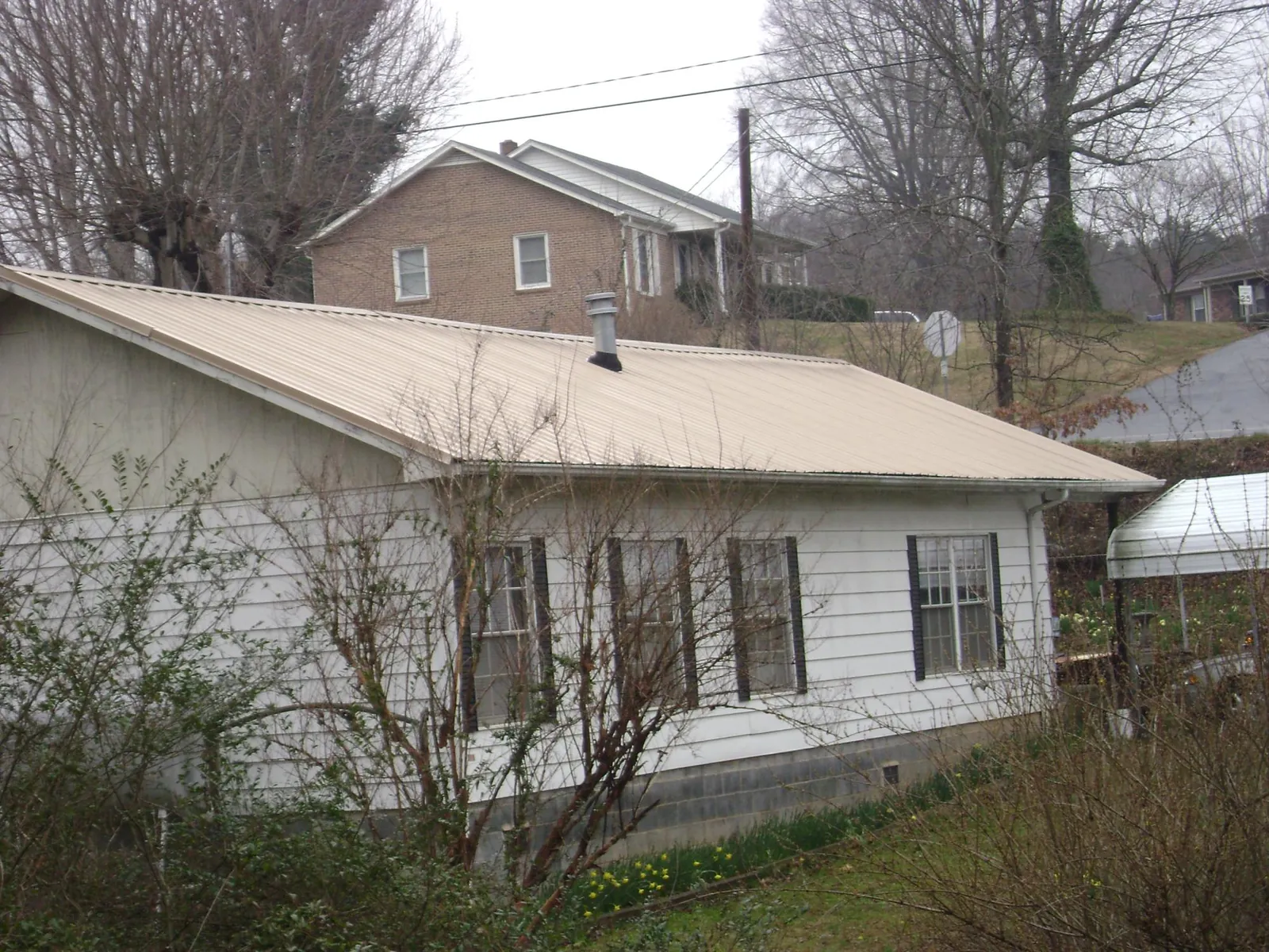 Tan metal roof on a white sided house set into a hillside — Commercial Roofing by Roofing Brothers in Evansville